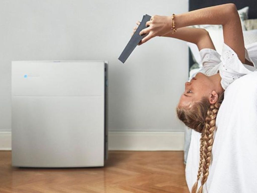 Teen girl laying upside down on her bed reading a book with a Blueair 605 air purifier nearby