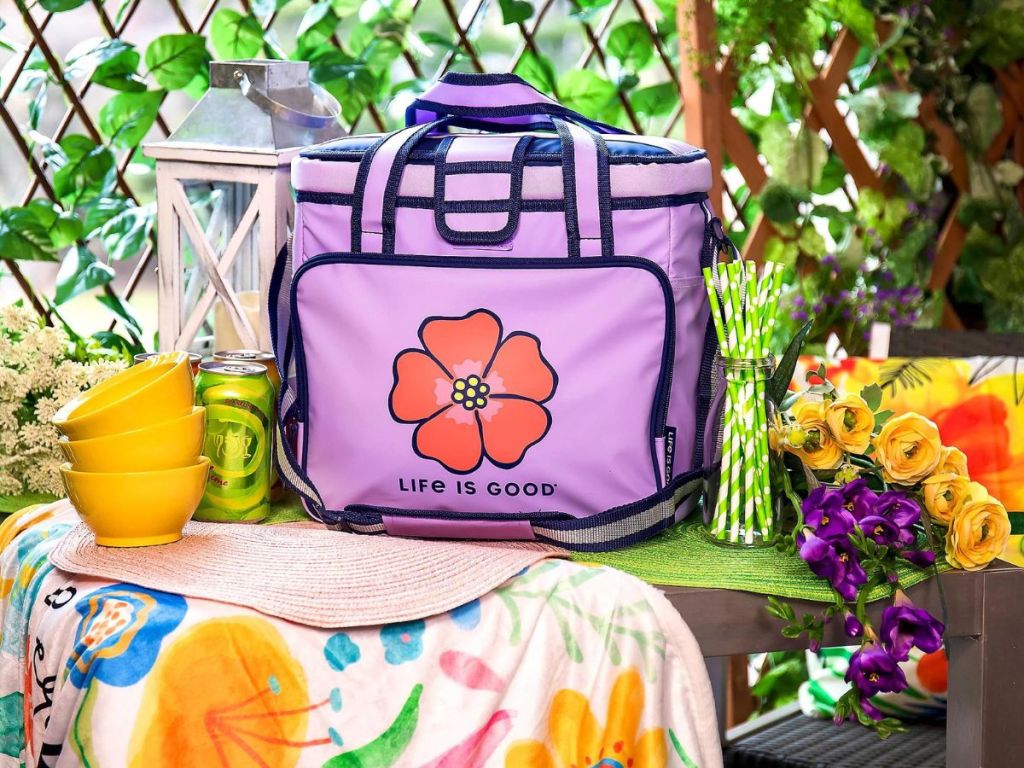 purple cooler with Life Is Good and flower graphic on table with yellow bowls, green straws, placemats and more 