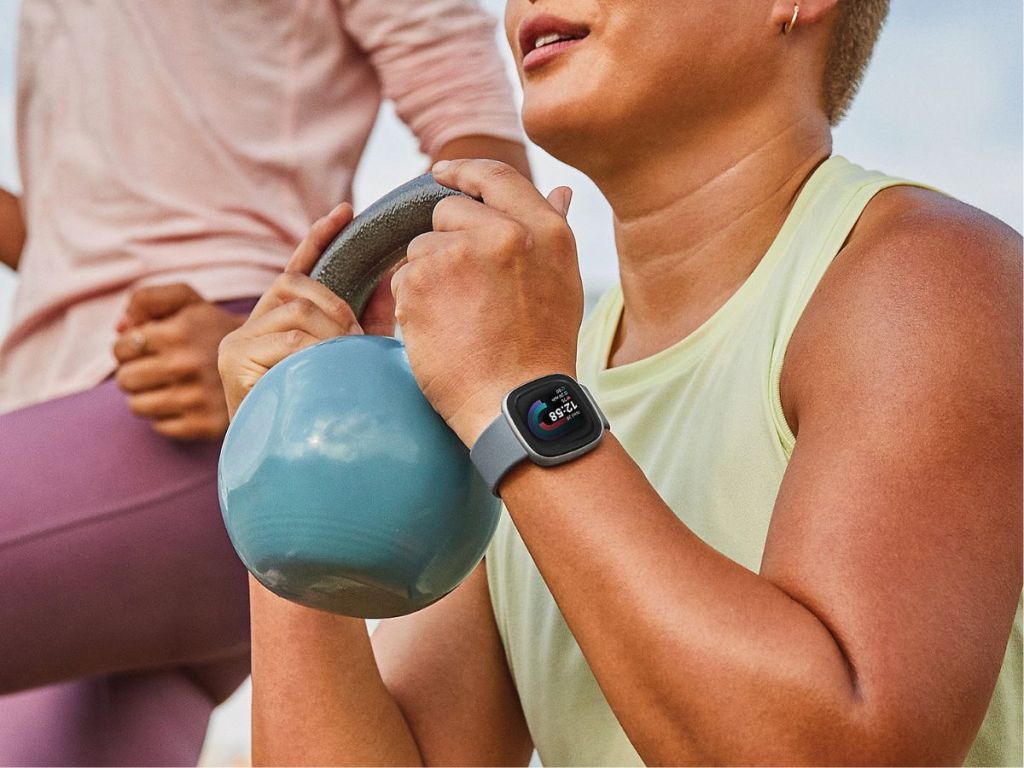 woman wearing green Fitbit watch lifting green kettlebell 