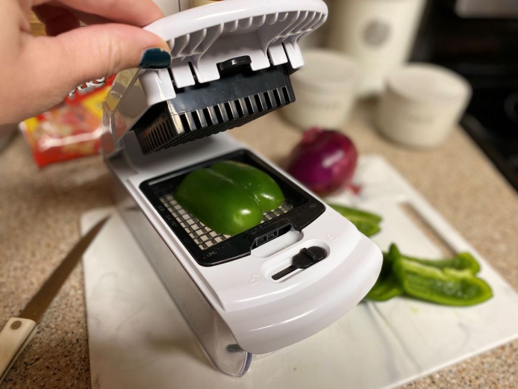 Hand holding open a vegetable chopper with a green pepper in it