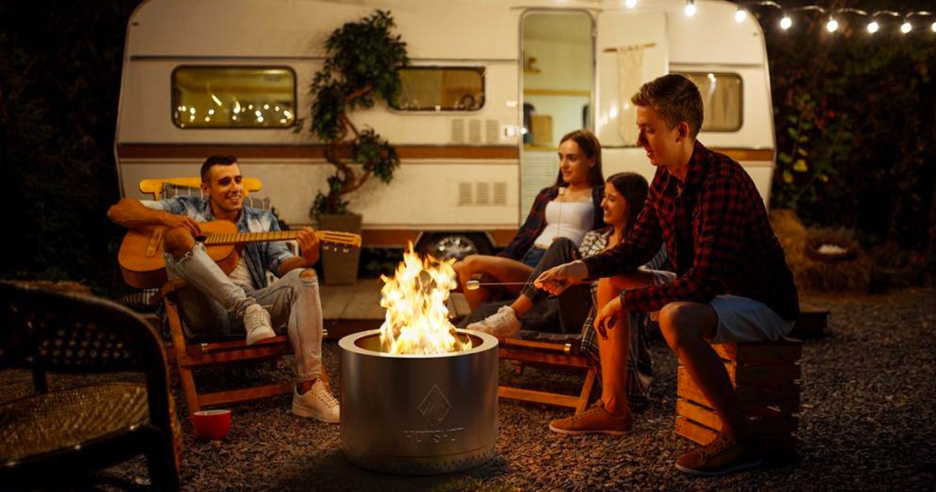 people sitting around a fire pit outside of a camper
