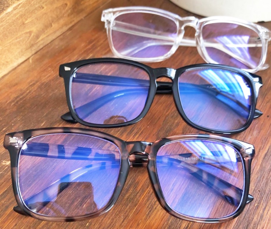 three pairs of blue light glasses on a wood table