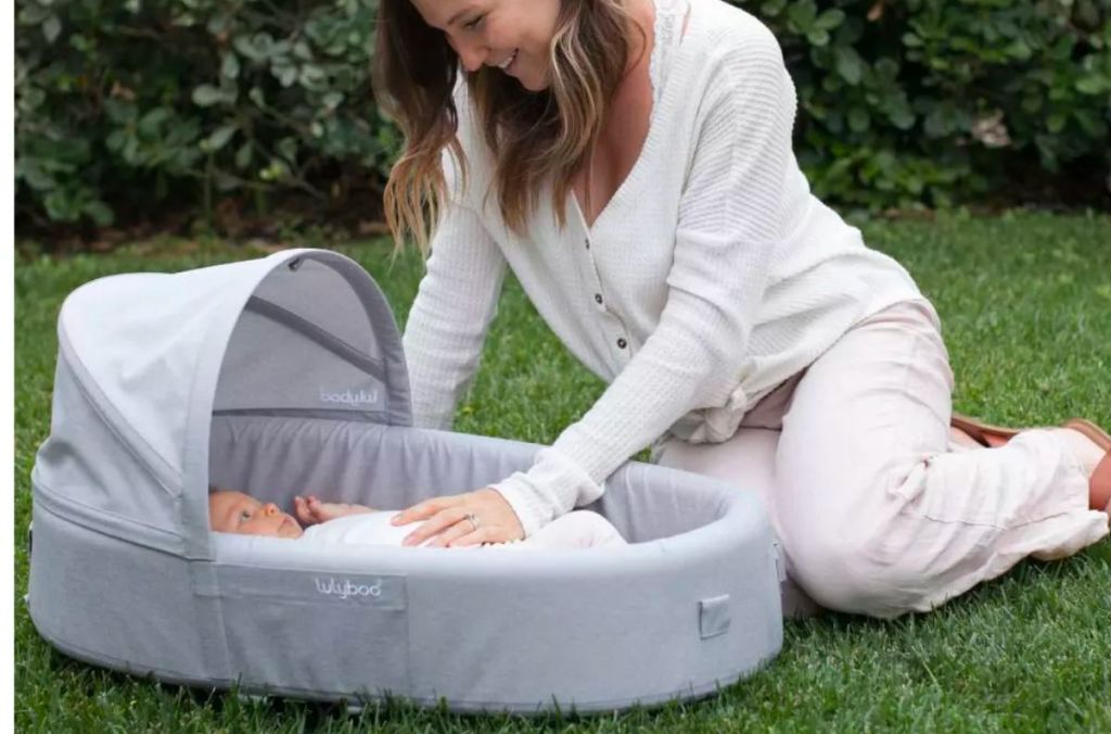 A mother with a baby sitting outside in a Lulyboo travel lounge and nest