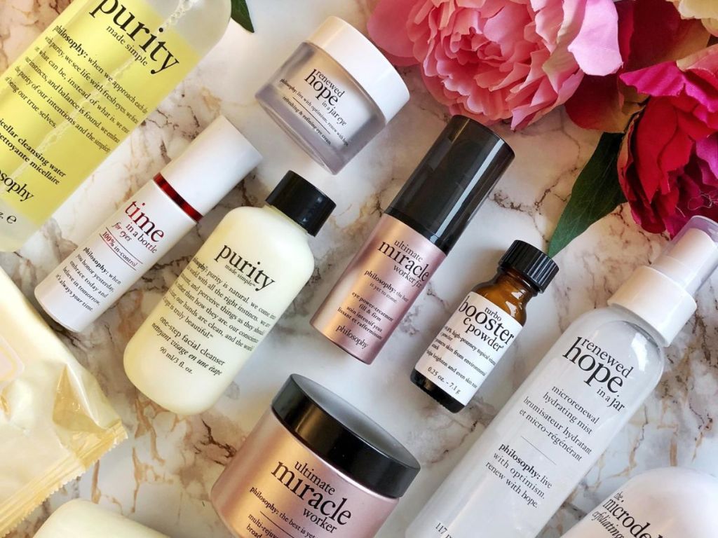 Group of philosophy skincare products laying next to fake flowers