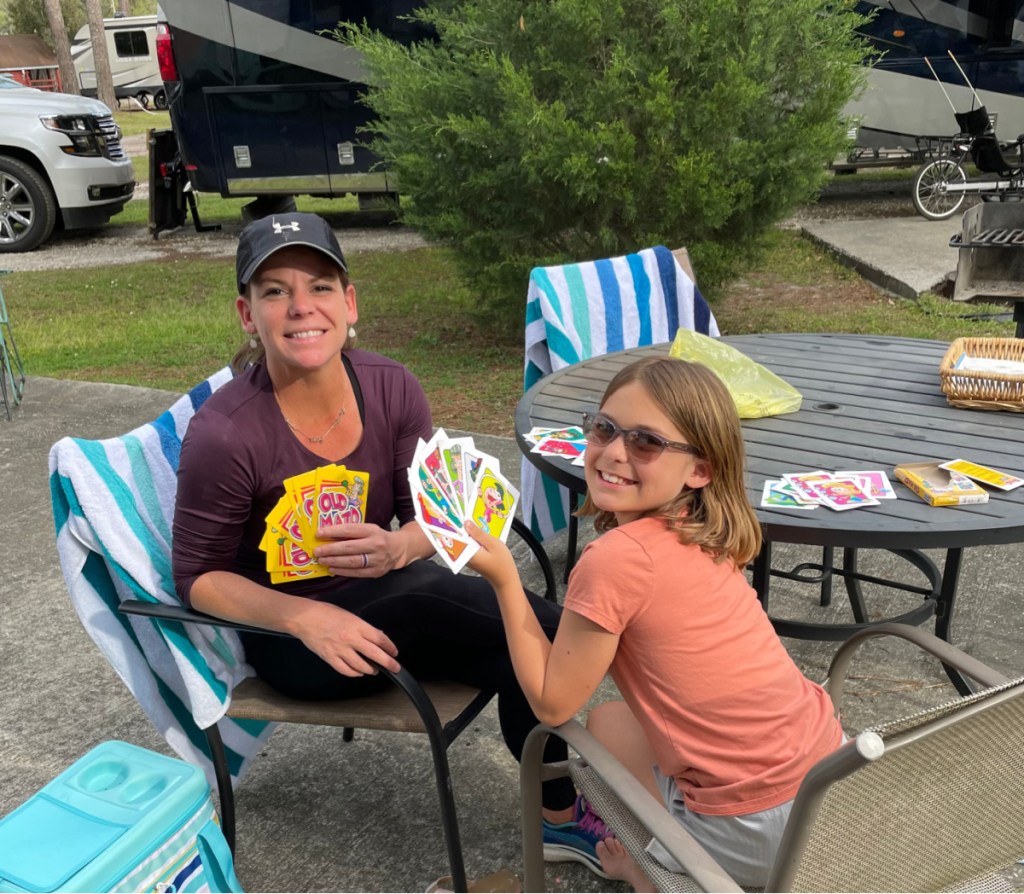 A mom and daughter playing cards outside at a camping table