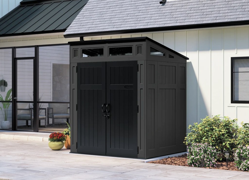 dark grey storage shed with black doors against a house