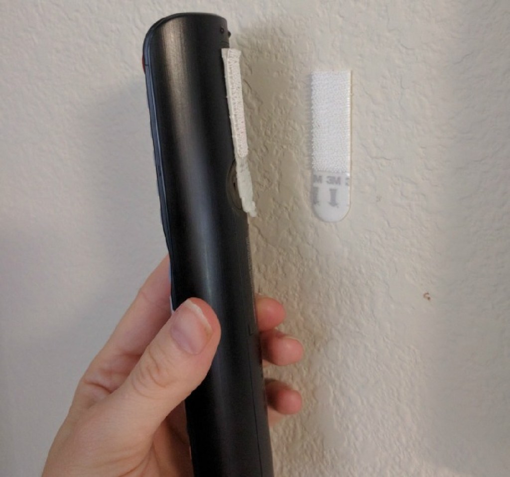 Hand attaching a remote control to a wall using velcro command strips