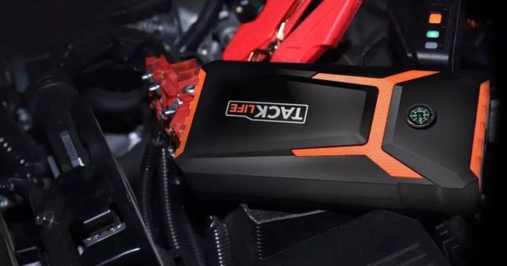 orange and black Tacklife jump starter hooked up to car battery