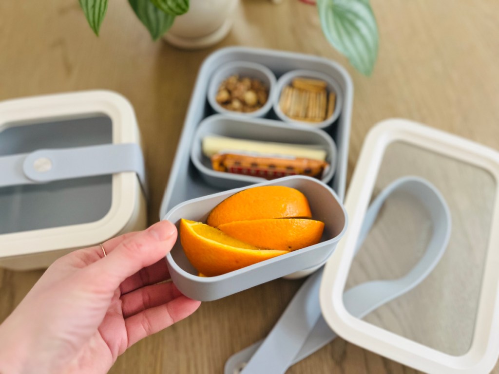 hand holding tray of oranges above other storage containers