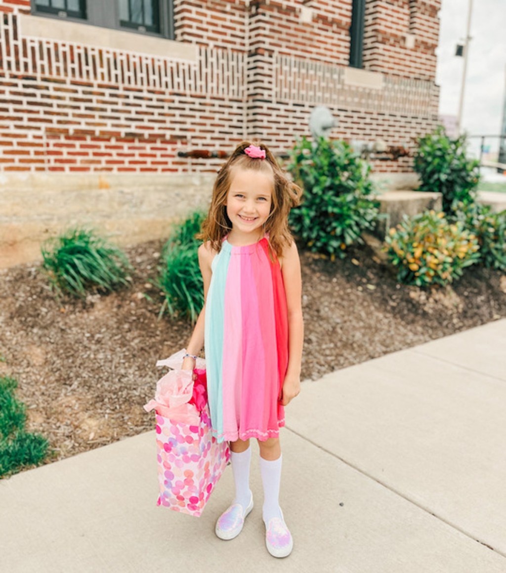 girl wearing colorful dress holding gift bag