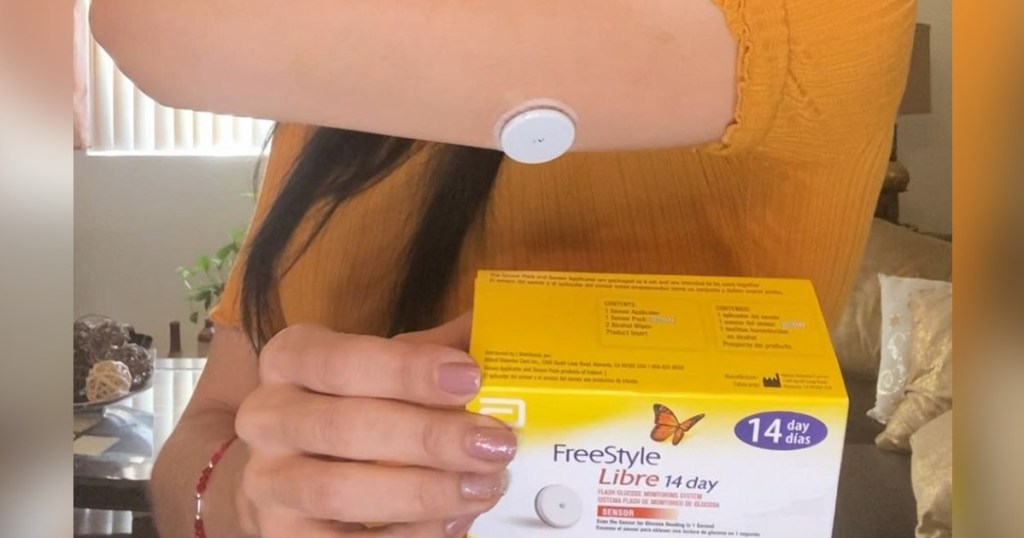 woman wearing continuous glucose monitor and holding product box