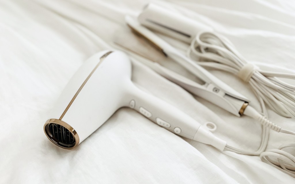 white hair dryer and straightener sitting on white bedding