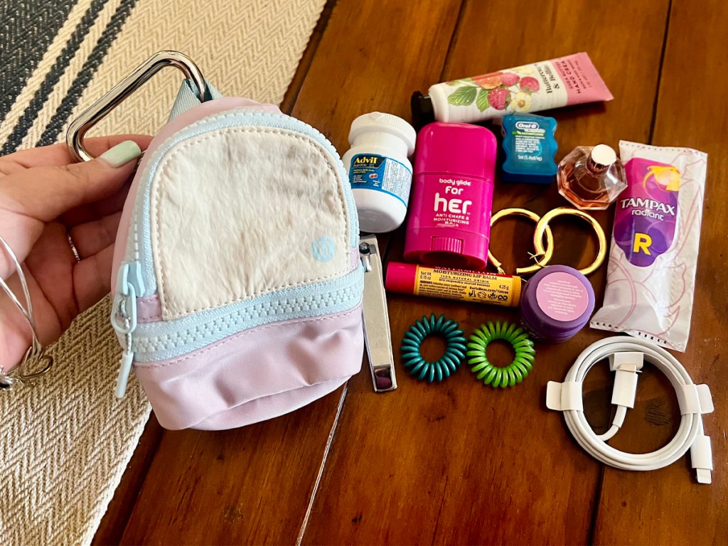 hand holding lululemon city adventure backpack on table with lots of personal items sitting next to it