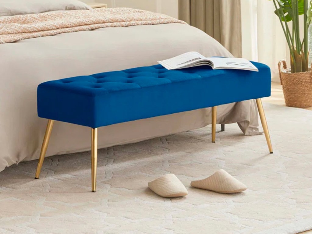 dark blue and gold bench in front of bed with book laying open on top