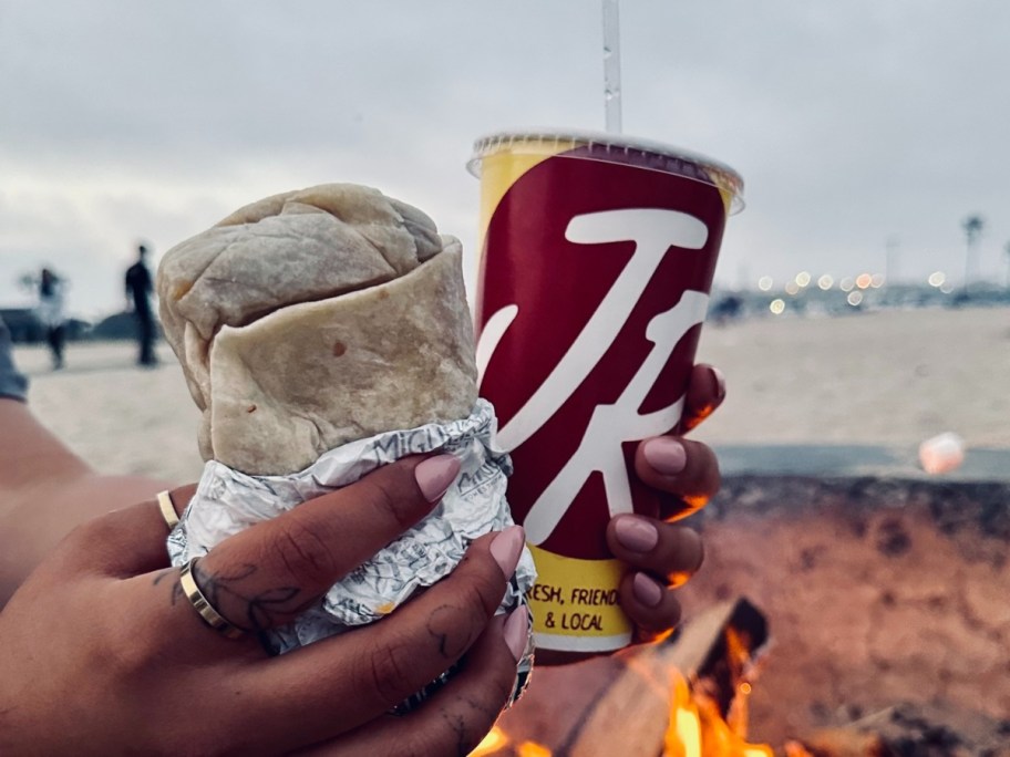 holding a burrito next to a Miguel's Jr. cup