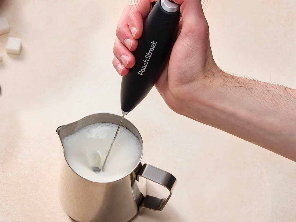 hand using milk frother in stainless steel cup