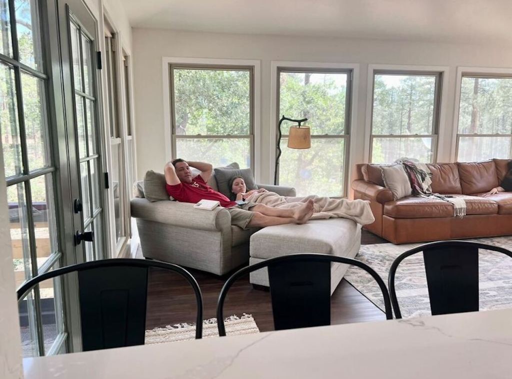 dad and daughter sitting on love chair in living room with tons of windows