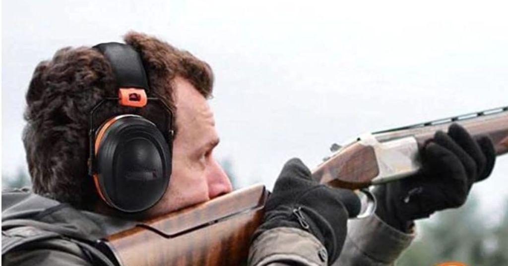 man wearing black and orange earmuffs shooting a rifle