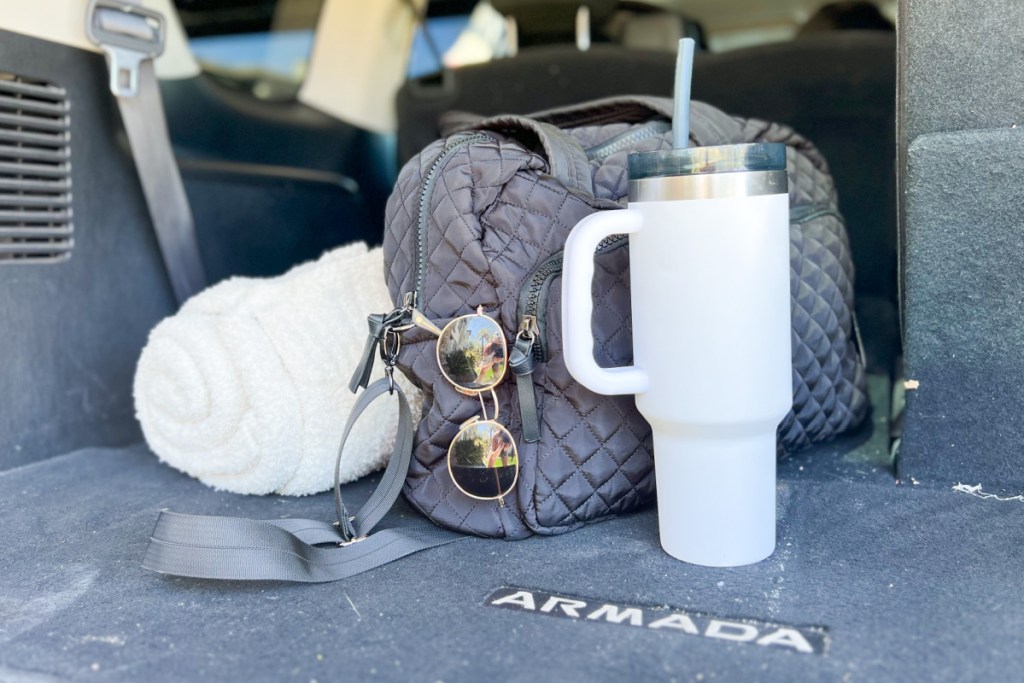tumbler weekender bag and white blanket sitting in the back of car