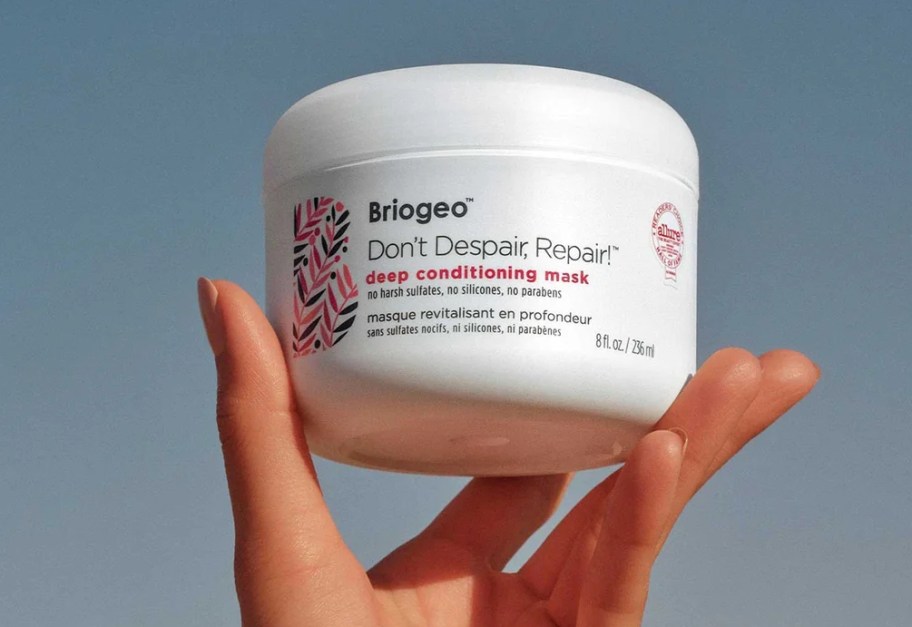 Hand holding a Briogeo Deep Conditioning Mask jar