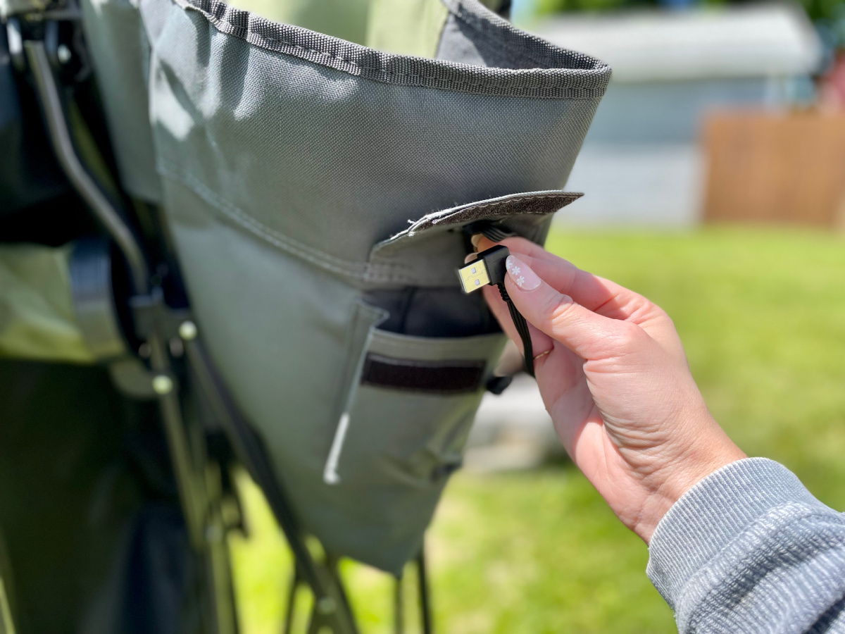 Woman putting a portable charger into the pocket on the back of her Backyard Expressions Heated Camp Chair