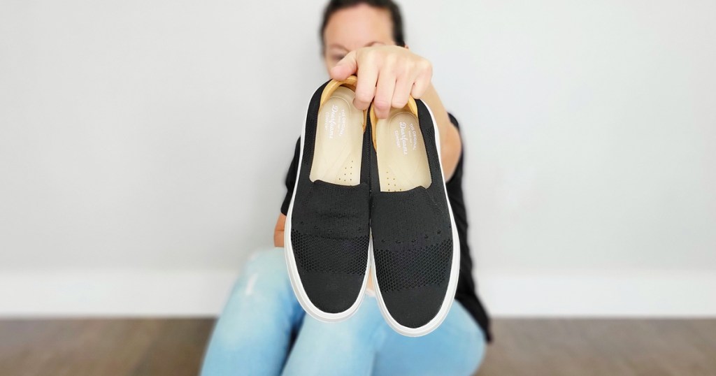 woman holding up a black pair of slip on sneakers