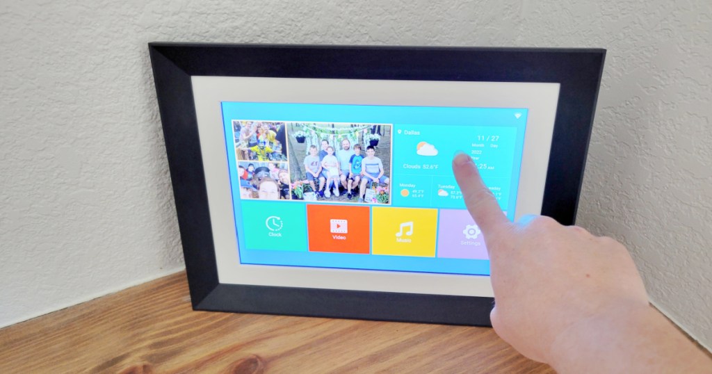 finger tapping screen on a digital photo frame displaying photos, the weather and other functions