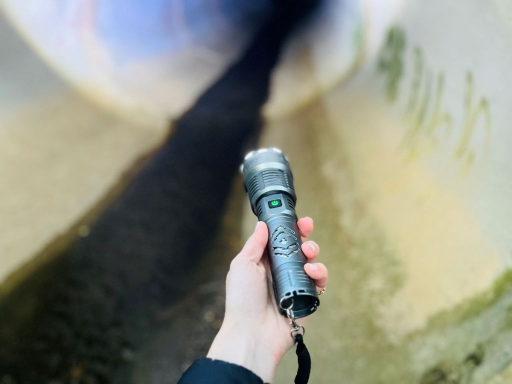 Hand holding a grey flashlight in a storm drain