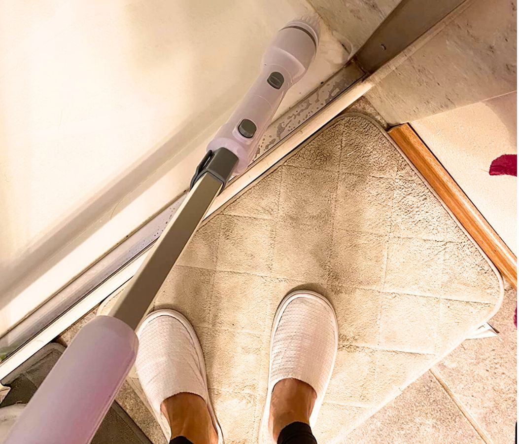 1st person view of woman using an electric scrubber to clean her shower