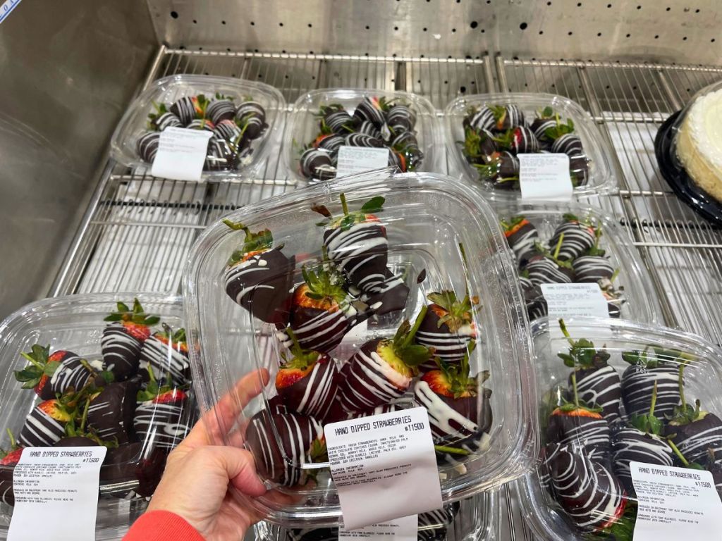 hand holding a plastic container of chocolate covered strawberries with more in the background at Costco