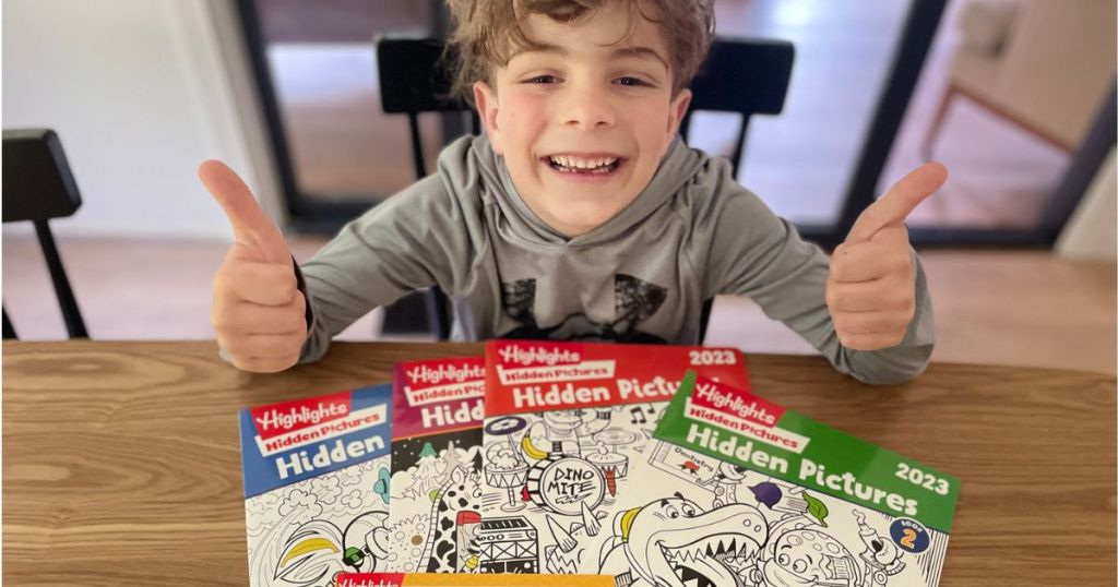 Little boy with 4 Highlights Hidden Picture Books in front of him while he gives two thumbs up