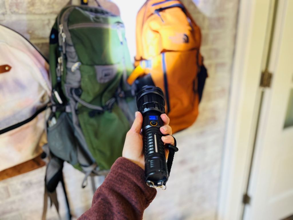 Hand holding a rechargeable flashlight near backpacks