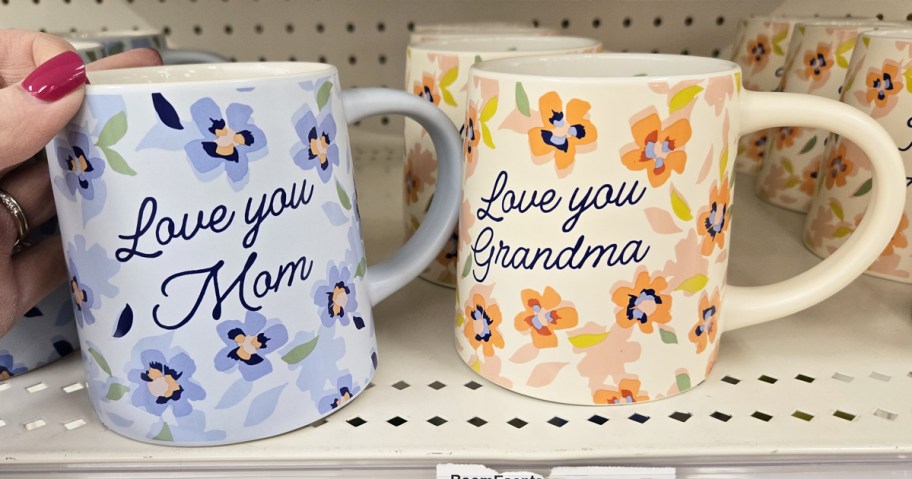 hand touching two floral print mugs on shelf that say "love you mom" and "love you grandma"