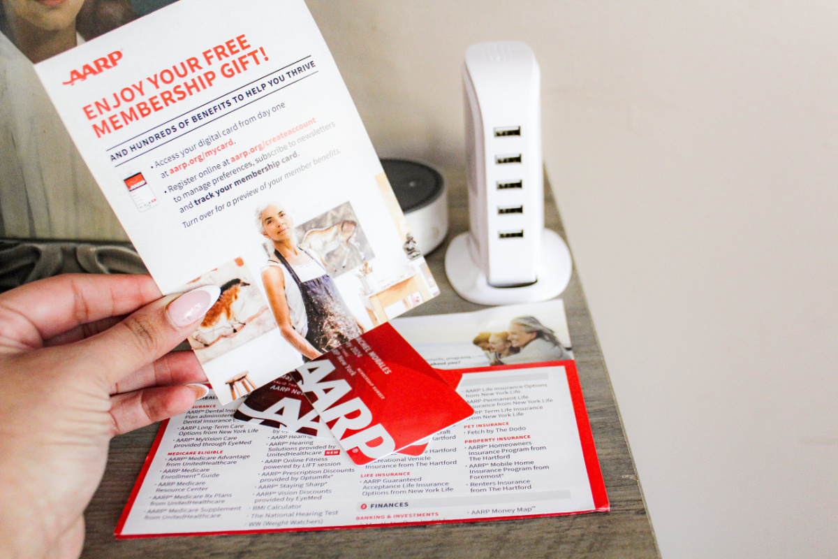 hand holding a welcome letter above aarp membership cards and a charging hub