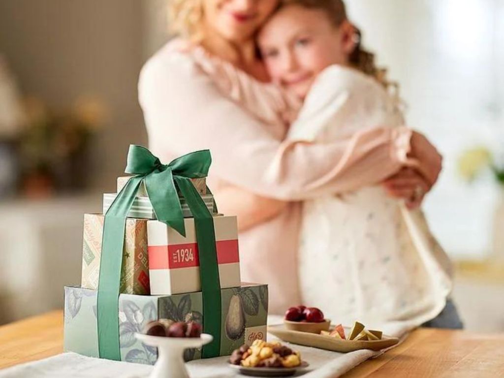 Harry & David Tower wrapped in a bow with bowl of cherries, stand with chocolate truffles and plate of Moose Munch next to it with woman and daughter hugging in background