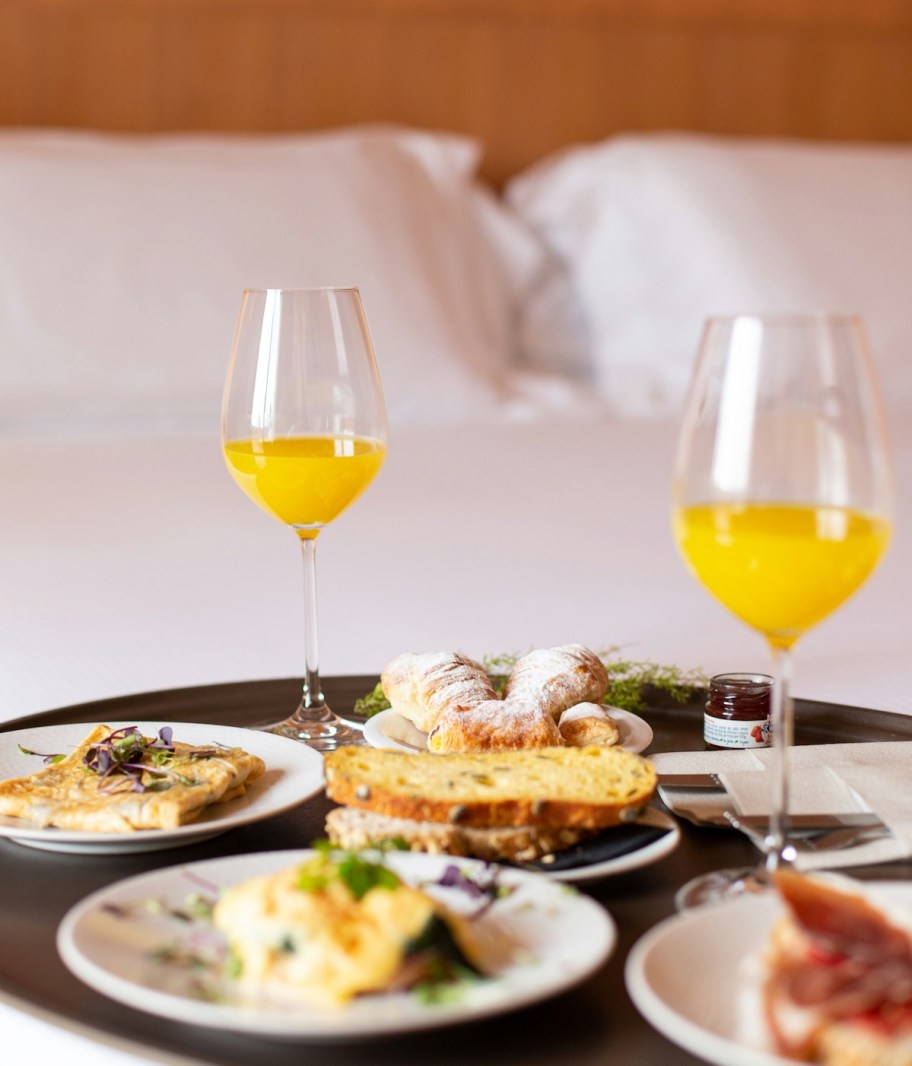 room service tray with food and orange juice in wine glasses on bed