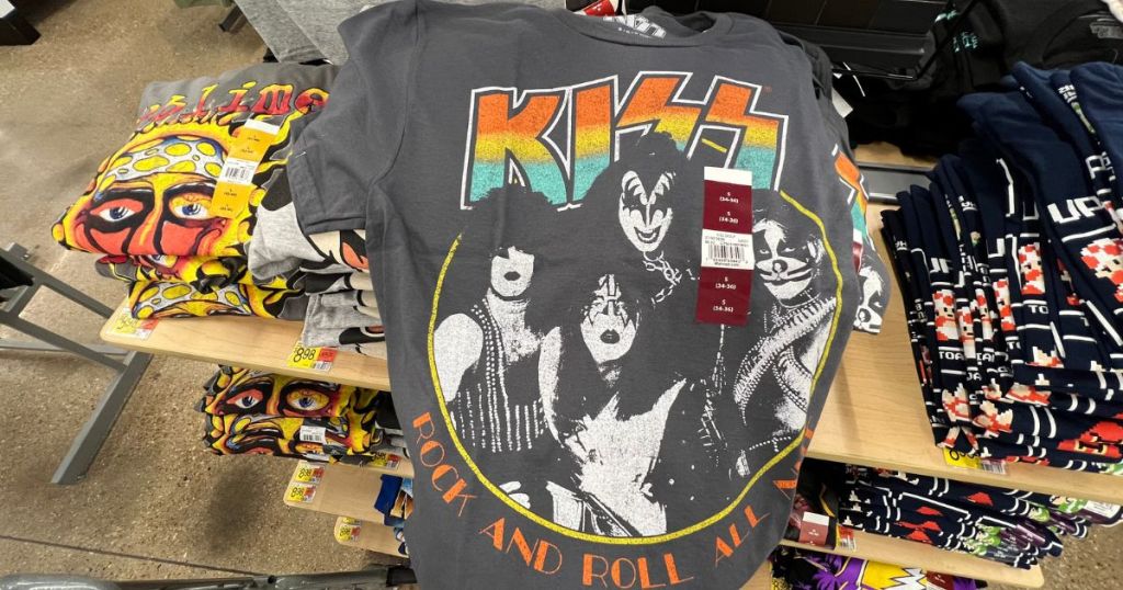 display table filled with graphic tees and person holding up Kiss tee