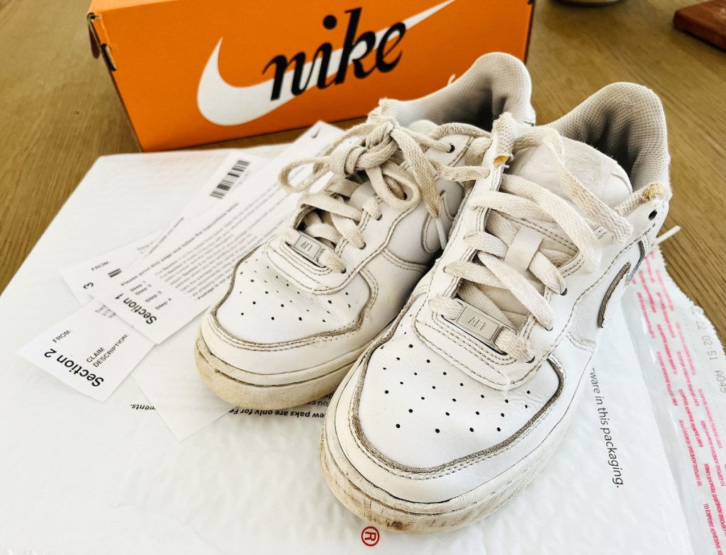 pair of dirty white nikes on table with nike claim warranty paperwork