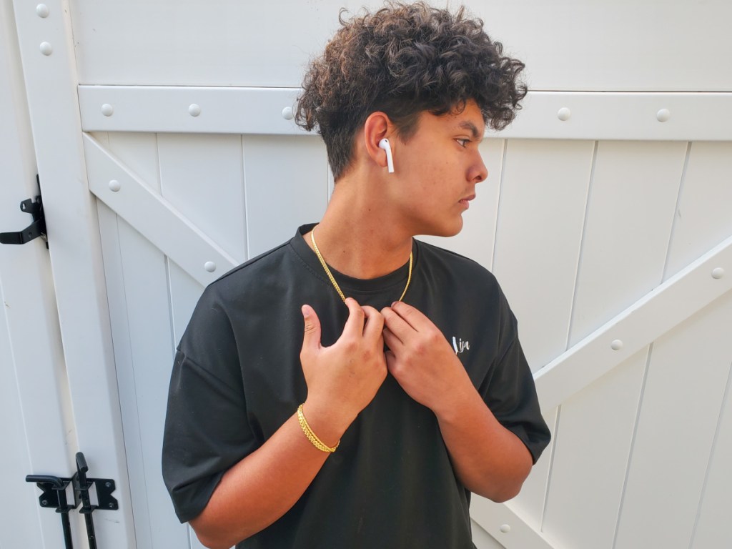 teenage boy in black shirt holding gold chain necklace and gold chain bracelet