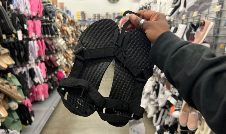 a womans hand holding a pair of black footbed sandals