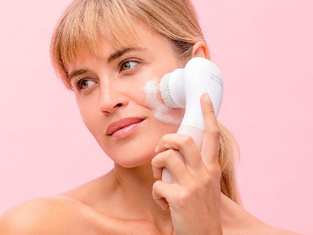 woman using facial cleansing brush to clean her face