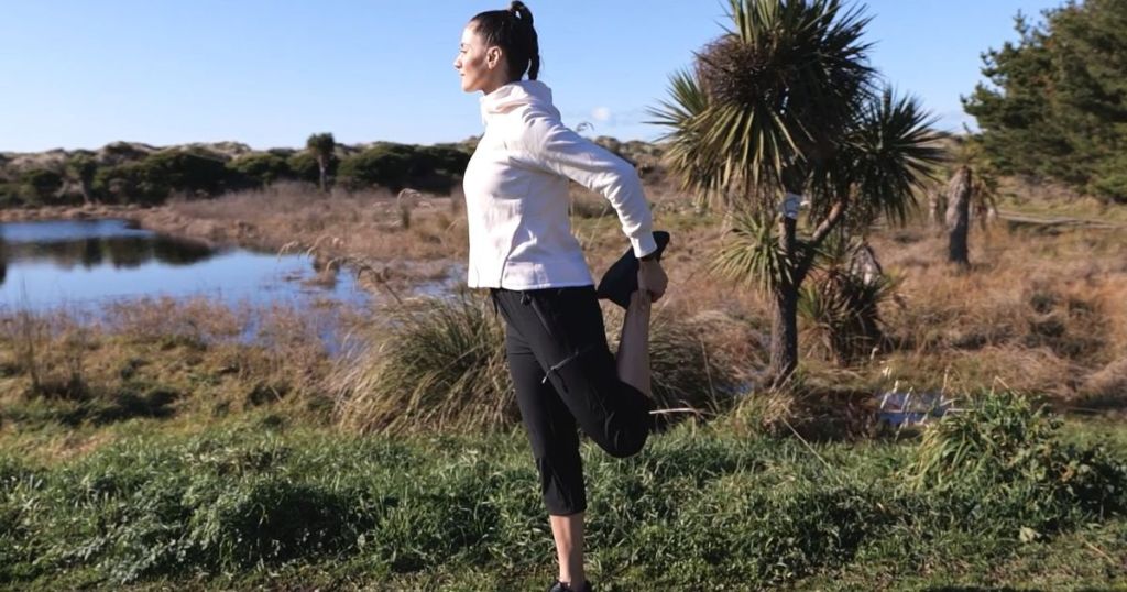 woman wearing white hoodie and black capri pants stretching her leg outdoors