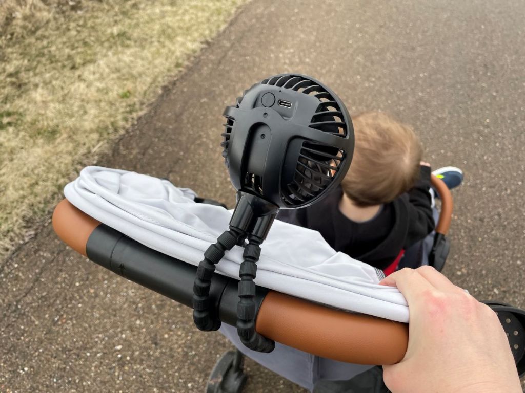 Hand pushing a stroller with a fan attached to the stroller