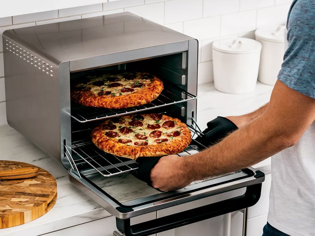 man removing two pizzas from a ninja oven