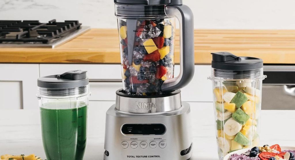 stainless steel ninja blender filled with fruit and single serve cups with fuit and green drink
