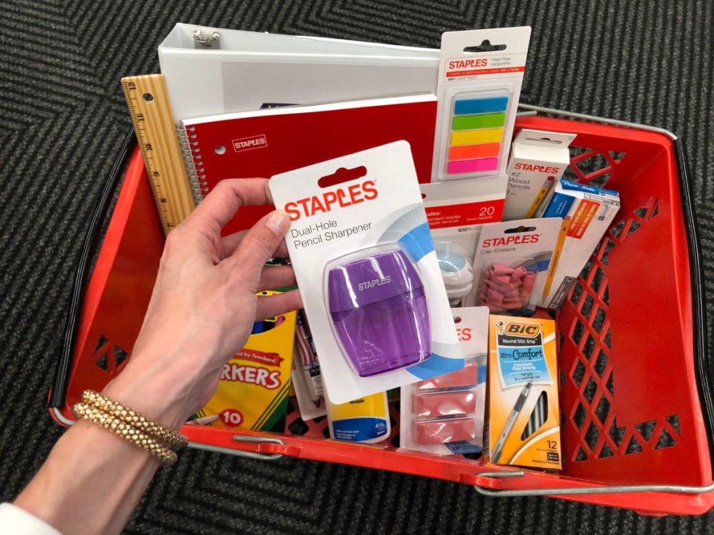 Hand holding a Staples pencil sharpener over a cart of Staples school supplies