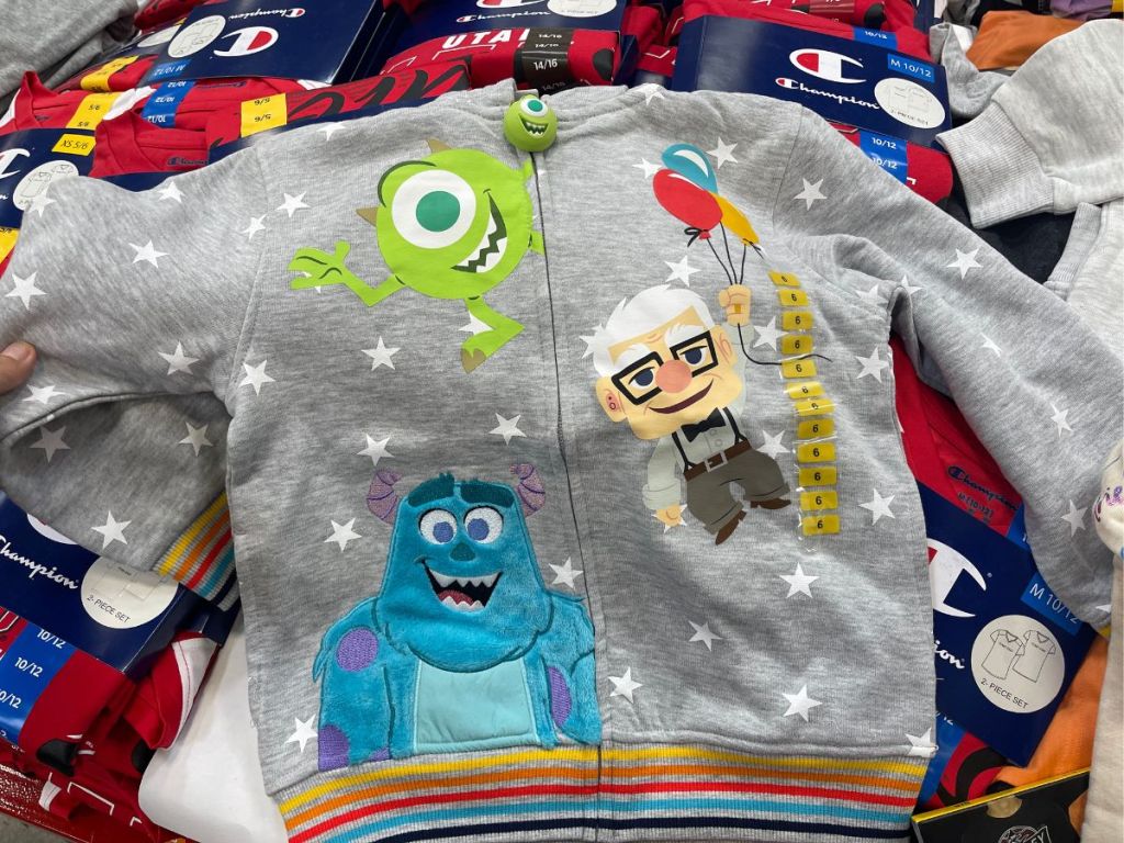 Monsters Inc and Up graphics zip up hoodie layed out on pile of clothes in store