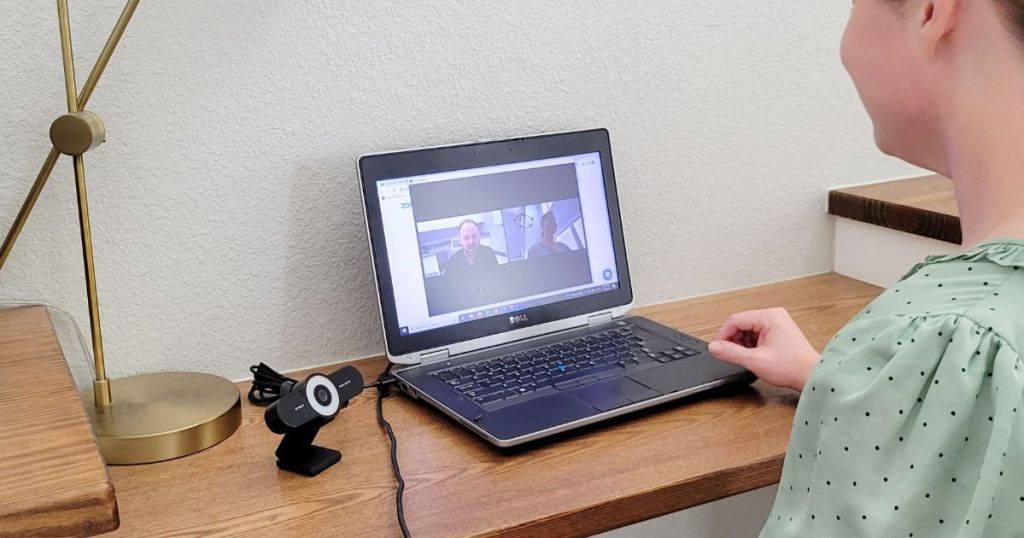 web camera next to laptop on desk with woman looking at laptop