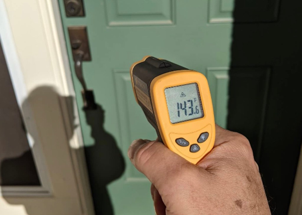 hand holding an infrared thermometer in front of green door - fathers day gift ideas