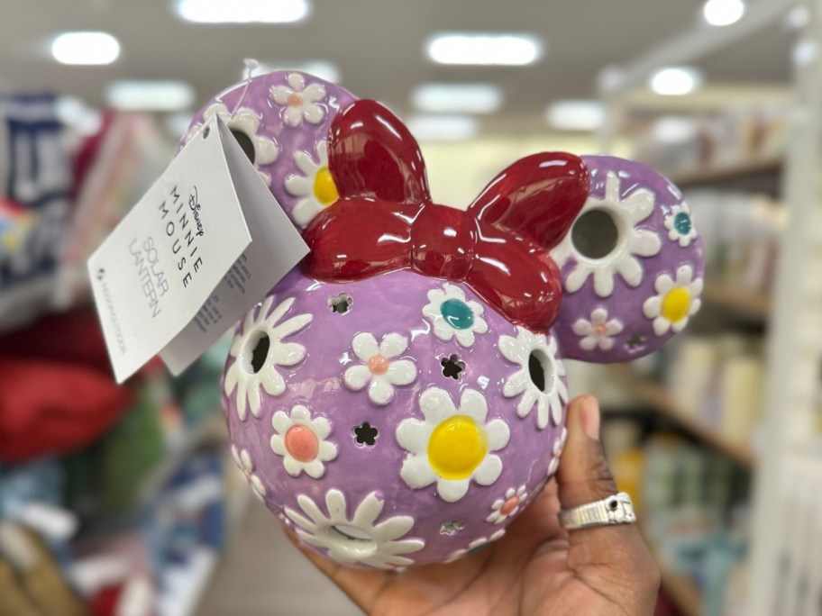 hand holding a Minnie Mouse head shaped ceramic solar lantern in purple with different color flowers on it and red bow